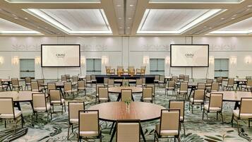 Un amplio salón de conferencias con varias mesas y sillas, un escenario y dos pantallas grandes mostrando 'OMNI'.