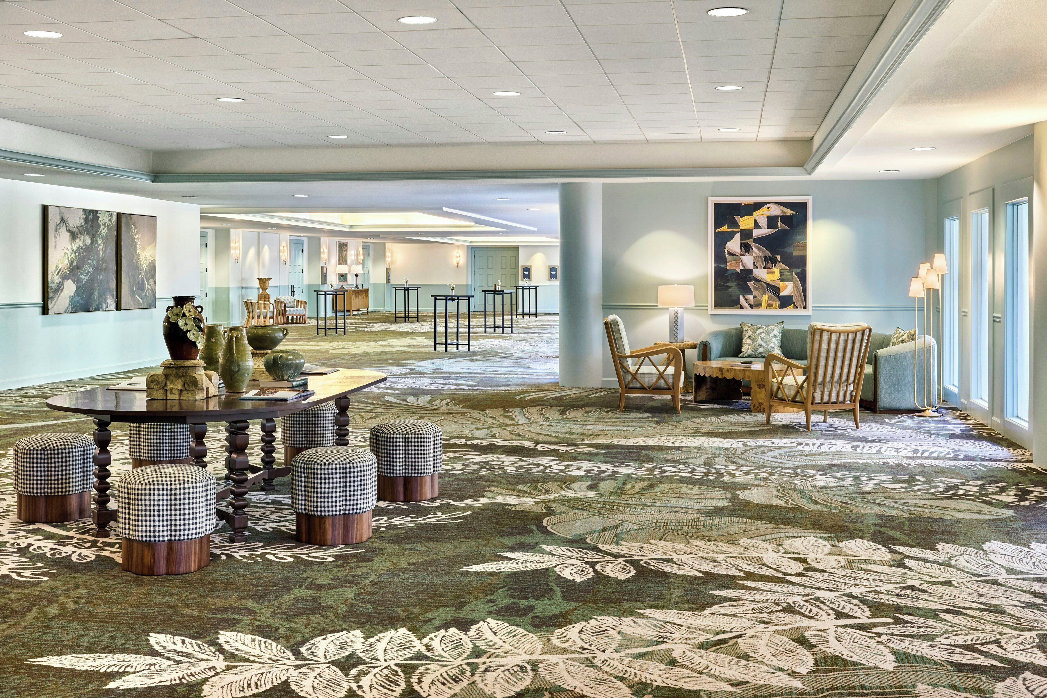 A hotel lobby with a round table, ottomans, chairs, artwork, and a patterned carpet.