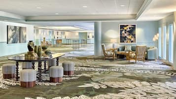 A hotel lobby with a round table, ottomans, chairs, artwork, and a patterned carpet.