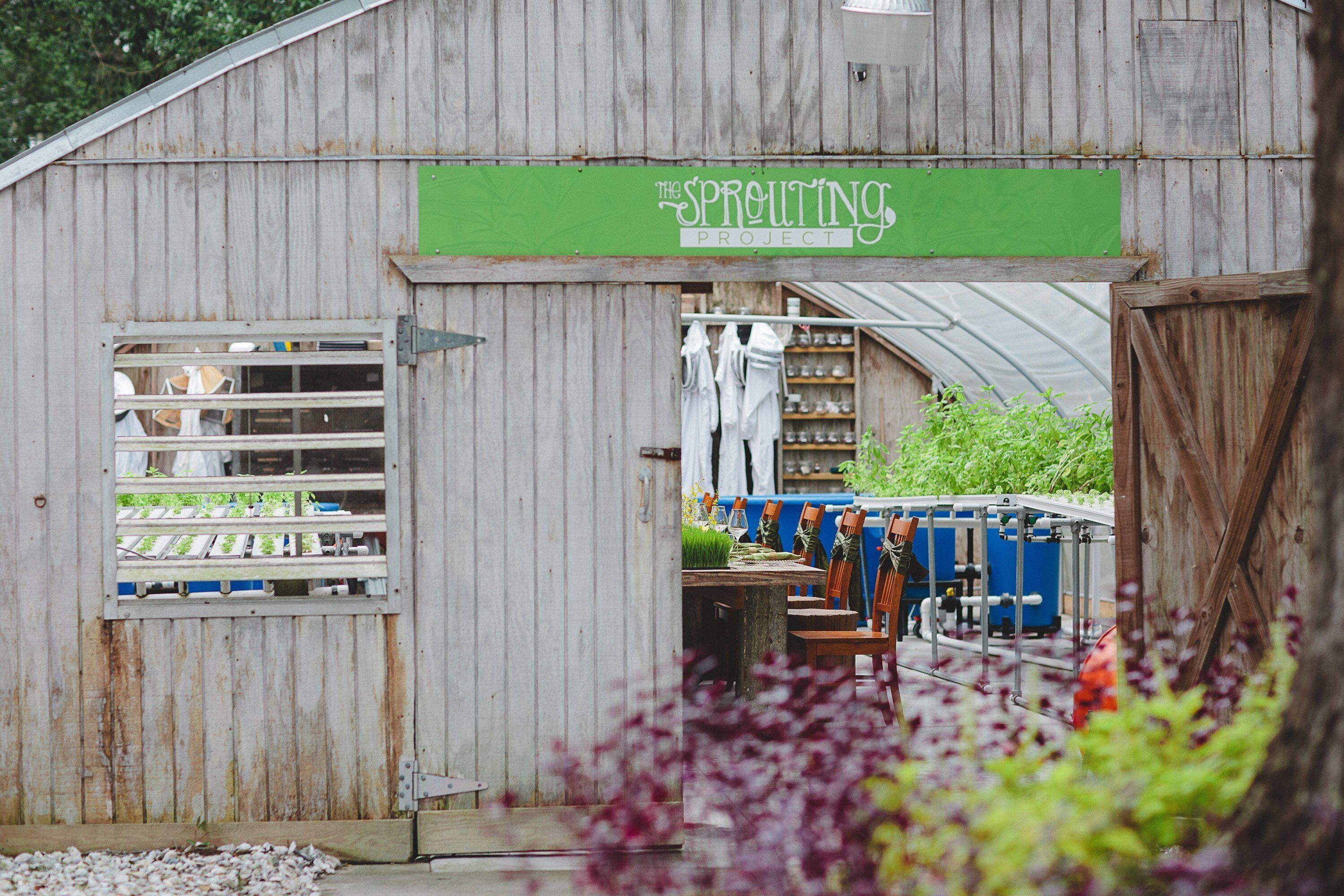 Un bâtiment rustique en bois, sur lequel on peut lire l’inscription « The Sprouting Project » sur une enseigne verte. À l’intérieur, on trouve des étagères remplies de bocaux et une table entourée de chaises.