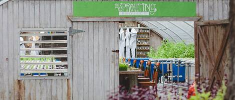 A rustic wooden building with a green sign reading 'The Sprouting Project'. Inside, there are shelves with jars and a table with chairs.