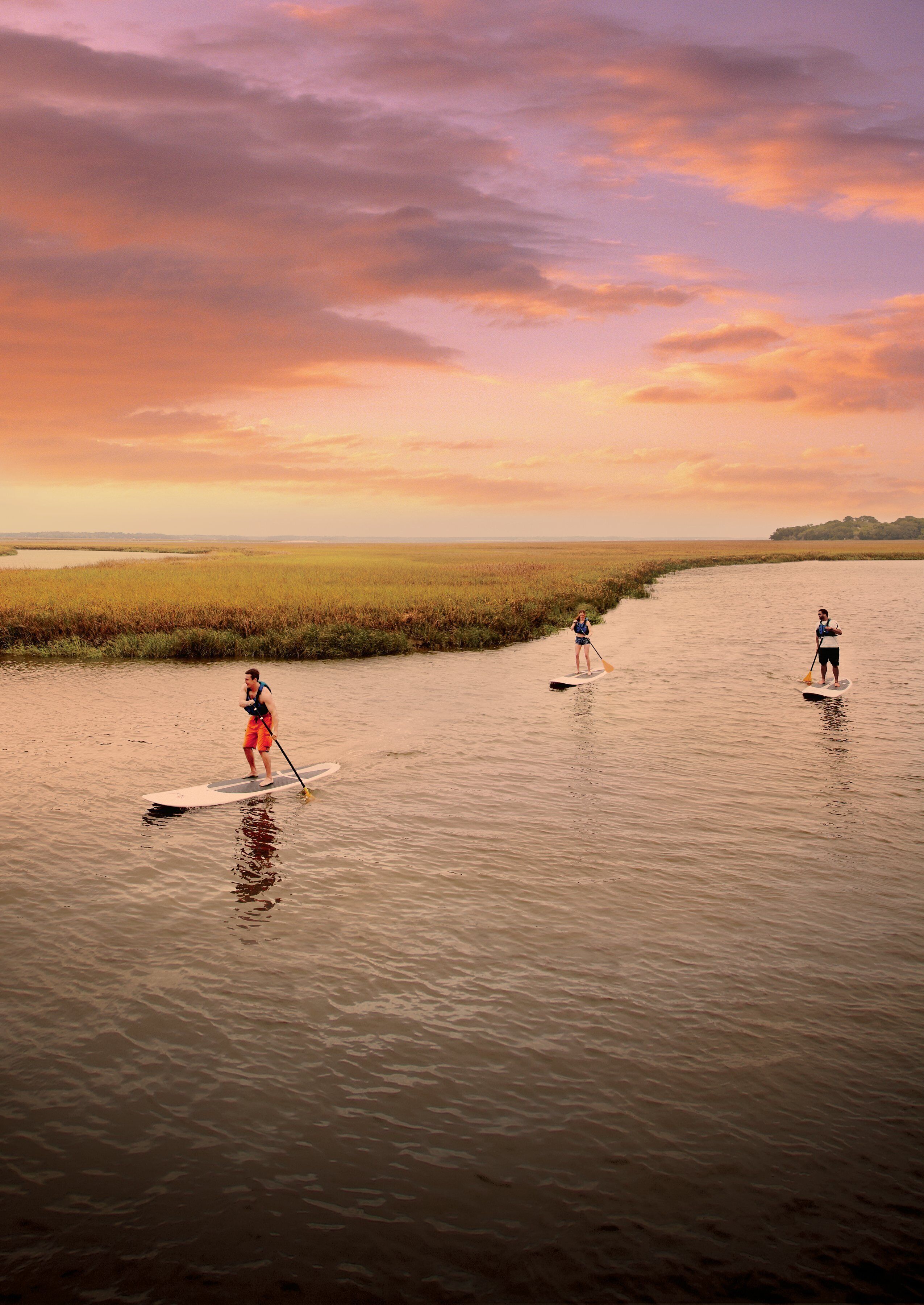 Una masa de agua tranquila con tres personas haciendo paddleboard.