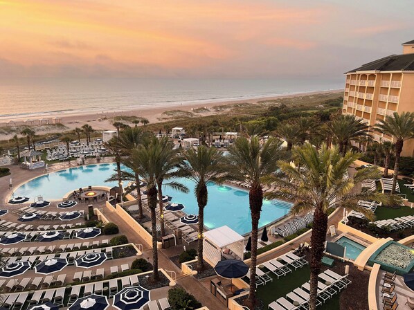 A resort with a large pool, sun loungers, and a view of the beach.