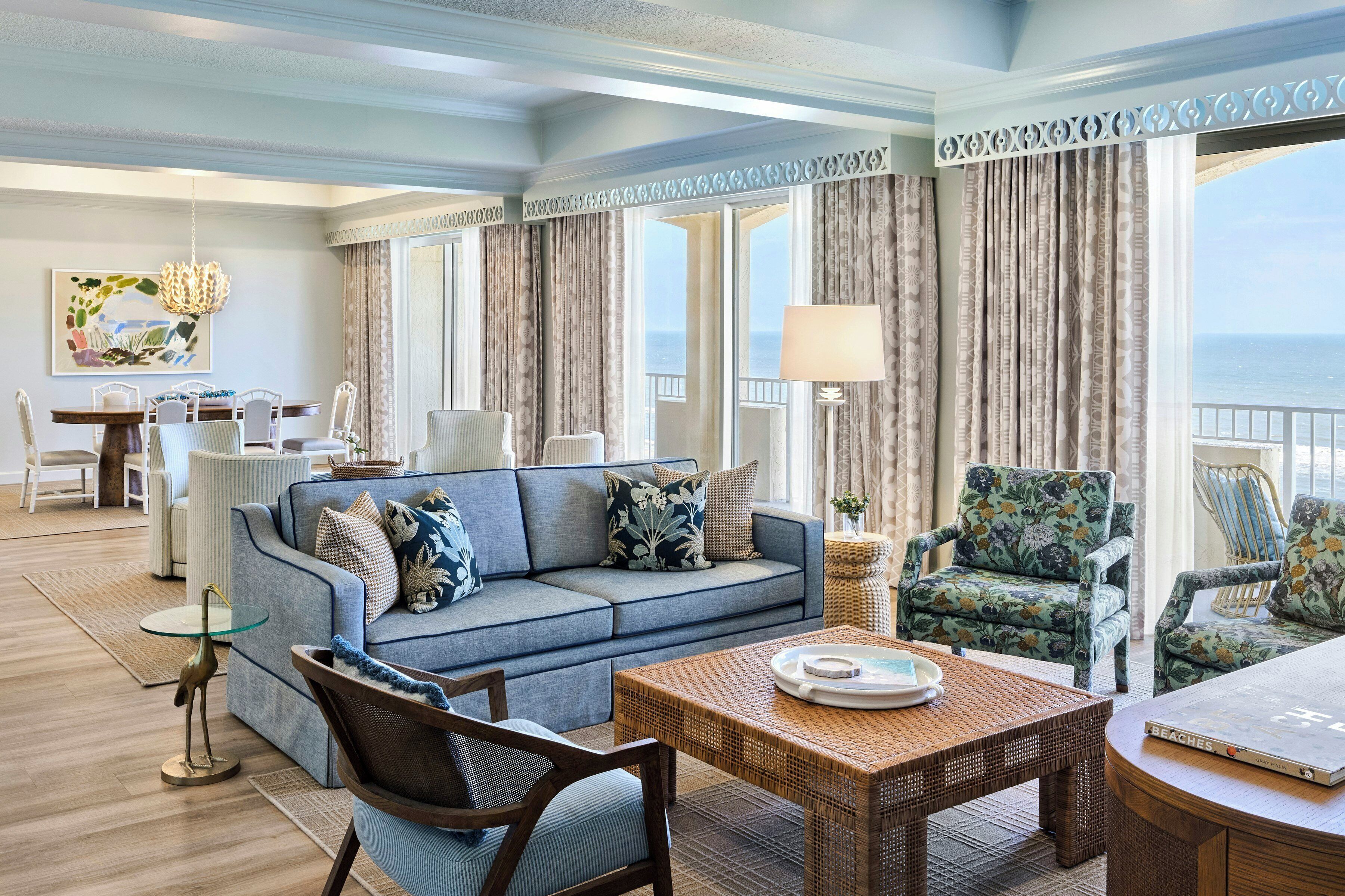 A spacious living area with a sofa, chairs, a dining table, and a view of the sea.