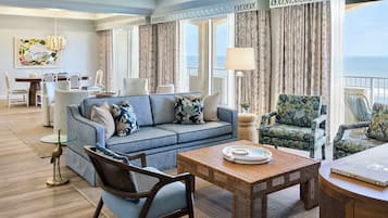 A spacious living area with a sofa, chairs, a dining table, and a view of the sea.