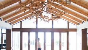 Un interior espacioso con un alto techo de madera y una gran lámpara de cristal hecha con ramas de madera natural.