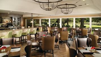 A restaurant with a bar area, multiple seating arrangements, and large windows offering a view of the outdoors.