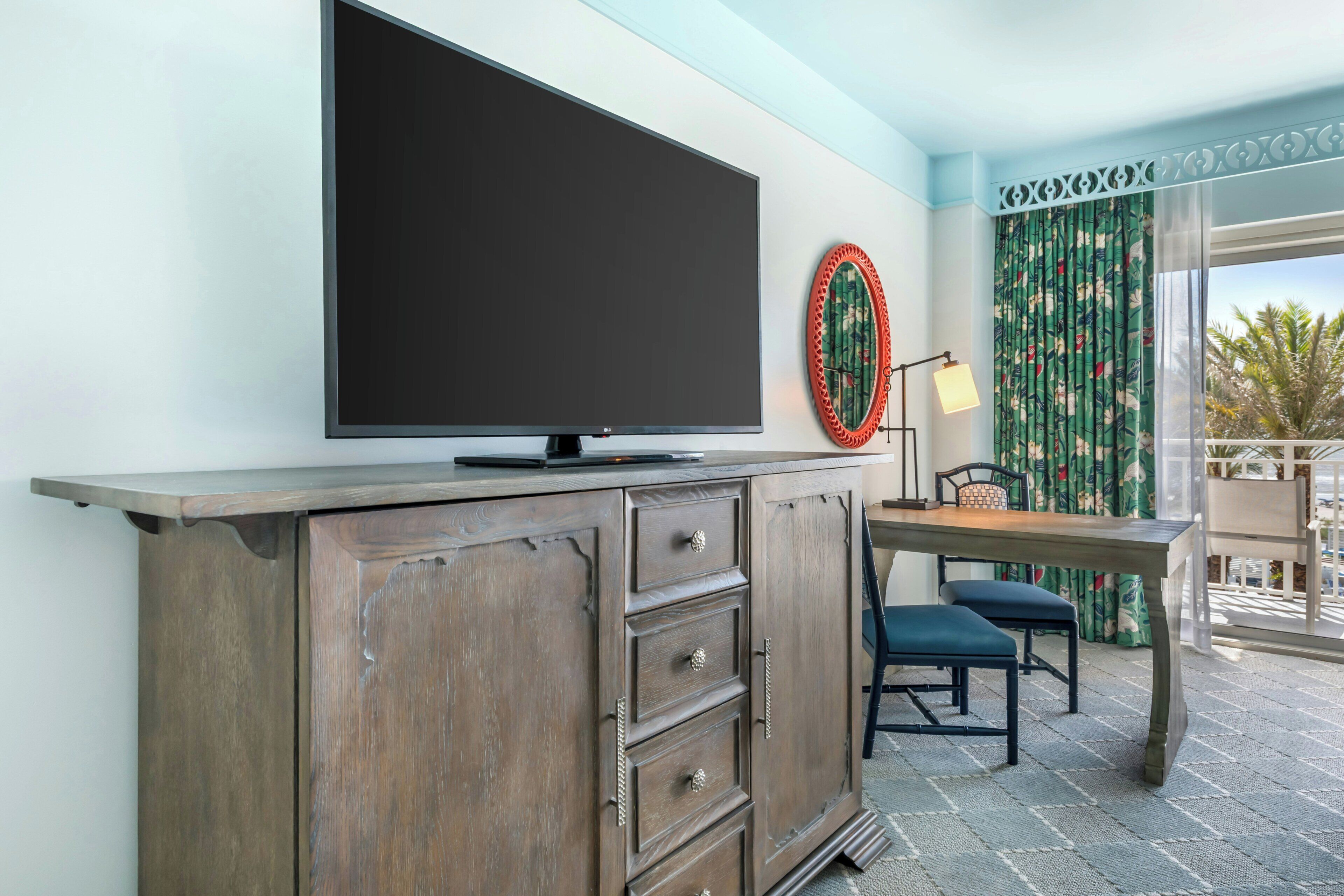 A flat-screen TV mounted on a wooden cabinet, a small table with chairs, and a decorative wall piece.