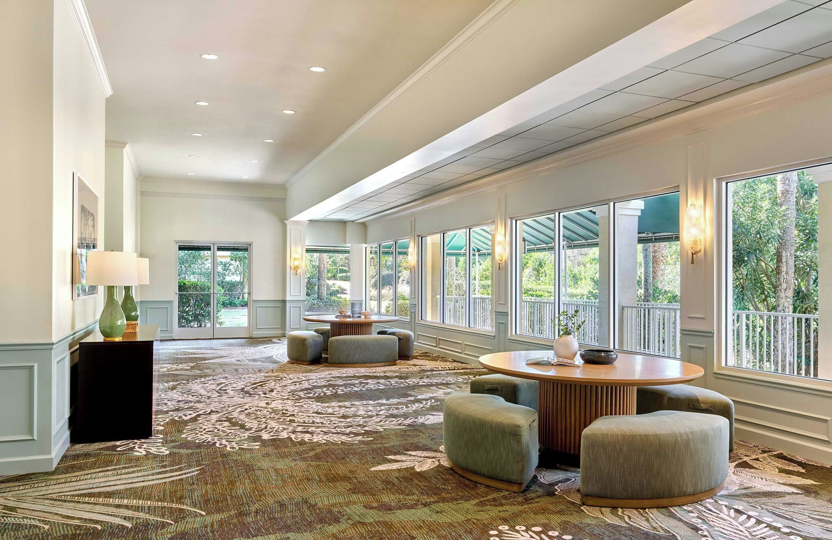 Eine geräumige Lobby mit großem Teppichbereich, Sitzgelegenheiten und großen Fenstern mit Blick auf Grünflächen.