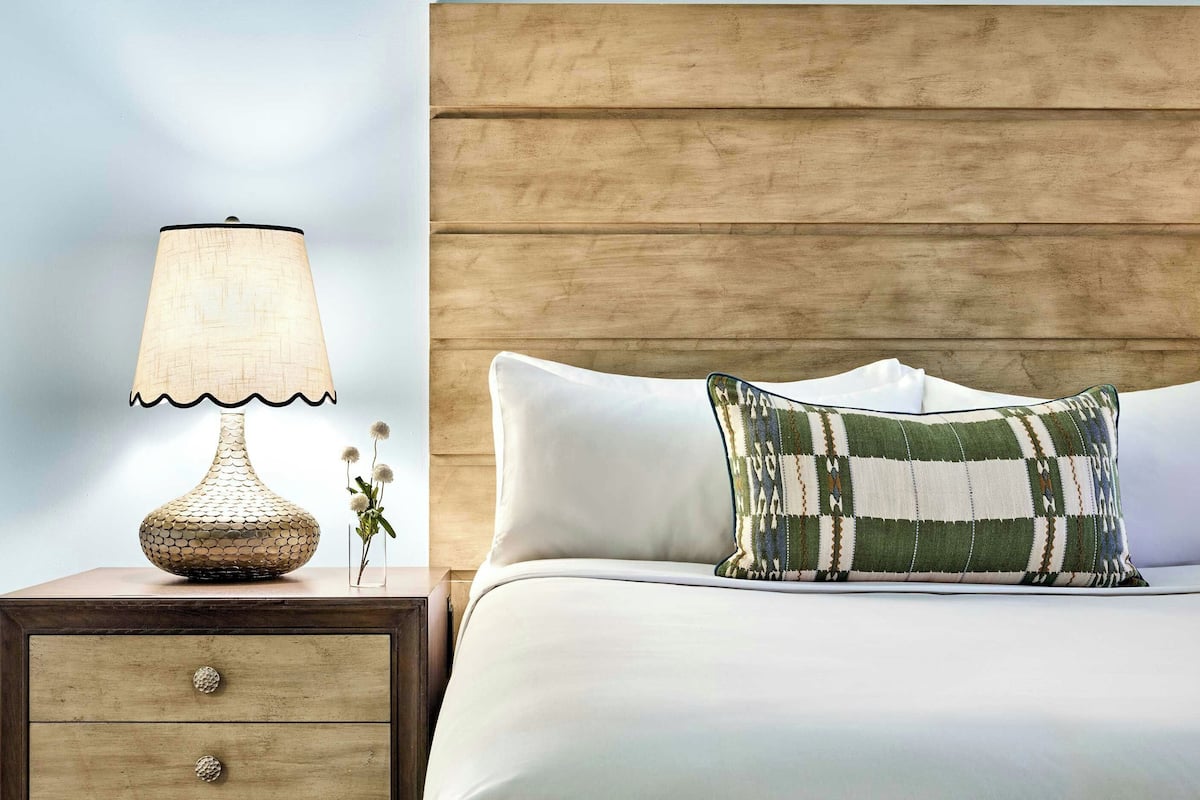 A neatly made bed with a patterned pillow, a bedside lamp, and a wooden nightstand with drawers.