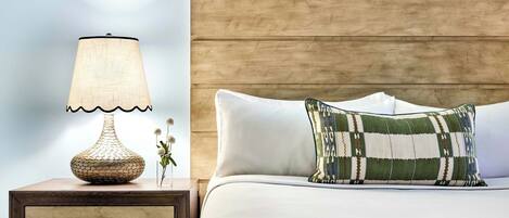 A neatly made bed with a patterned pillow, a bedside lamp, and a wooden nightstand with drawers.