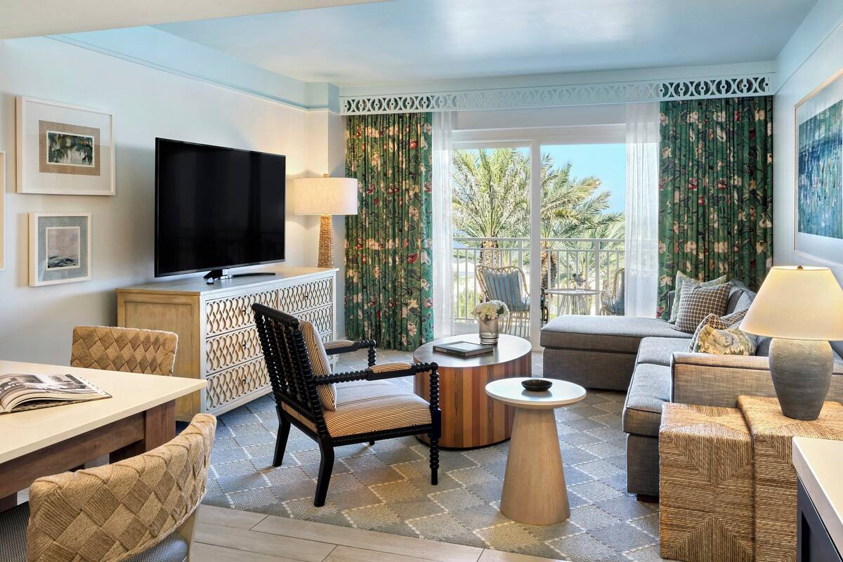 A living room with a TV, sofa, armchair, coffee table, and a balcony with curtains.