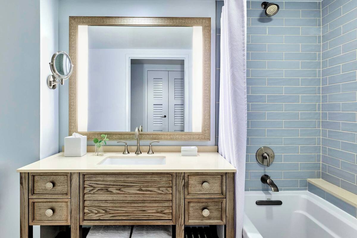 A bathroom with a wooden vanity, a large mirror, a sink, and a shower area with blue tiles.