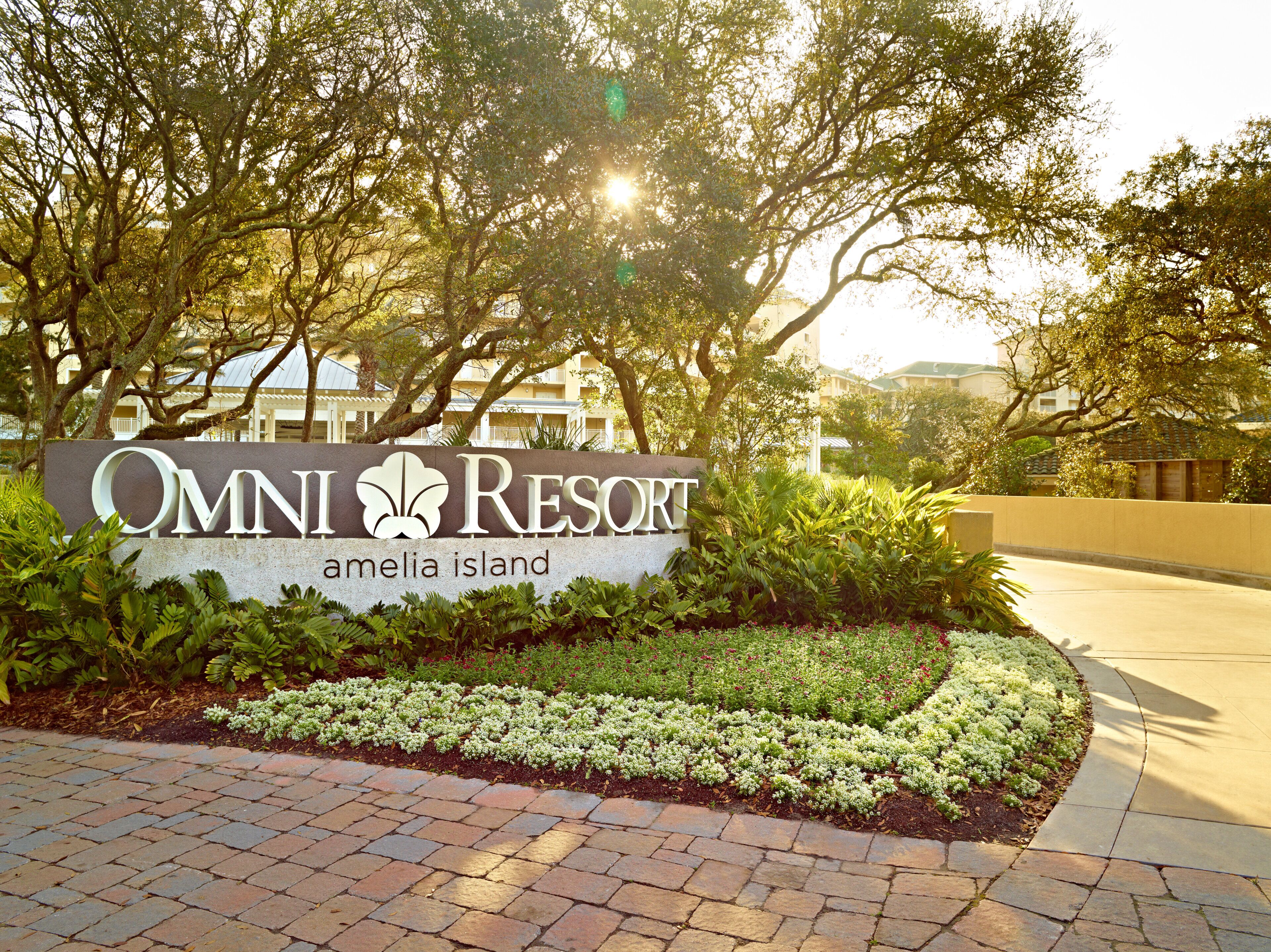 A sign for Omni Resort Amelia Island with a paved walkway and greenery.