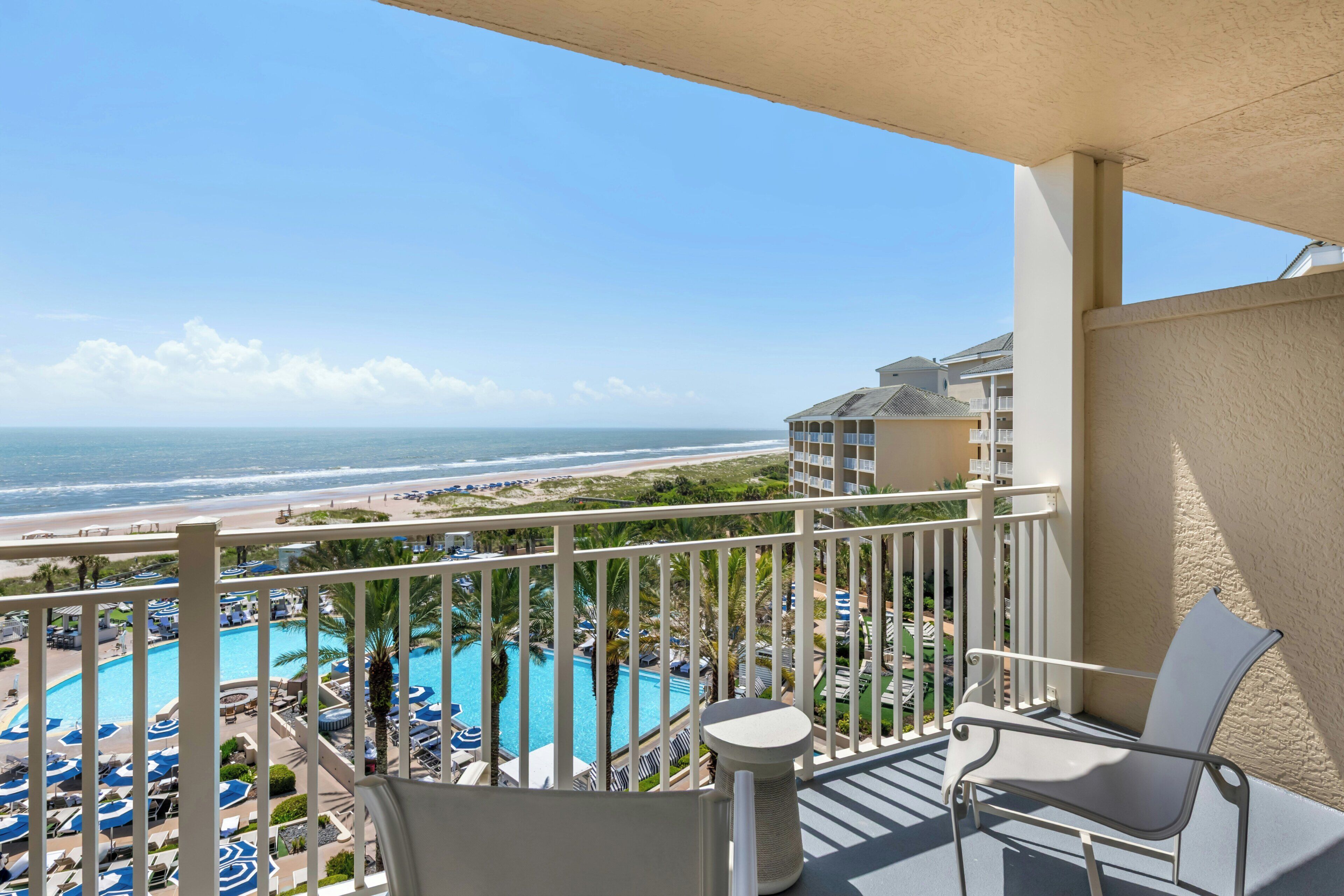 A balcony with a view of a beach and a pool area.