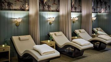Un cuarto de spa con cuatro sillones reclinables, cada uno con una toalla, una mesita con una vela y lámparas de pared.