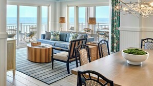Amplia sala de estar con vista al océano, un comedor con mesa de madera y una zona de estar con sillas de mimbre.