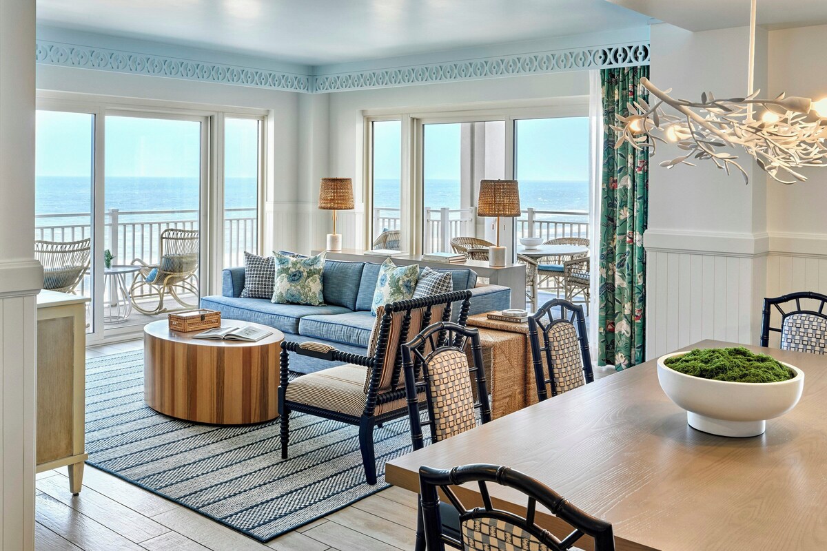 Amplia sala de estar con vista al océano, un comedor con mesa de madera y una zona de estar con sillas de mimbre.