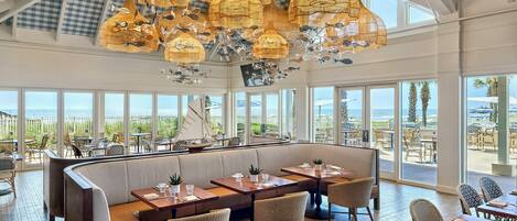 A restaurant with a high ceiling, large windows, and a view of the ocean.
