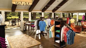 A clothing store with racks of shirts, a wooden floor, and a large window overlooking a garden.