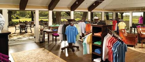 A clothing store with racks of shirts, a wooden floor, and a large window overlooking a garden.