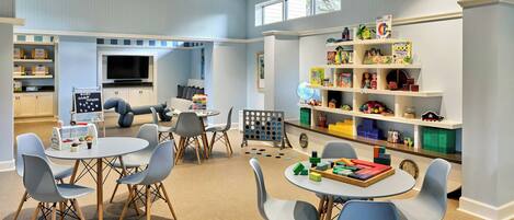 A children's playroom with a TV, shelves with toys, and a table with chairs.