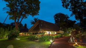 A thatched-roof building with outdoor seating, surrounded by lush greenery and palm trees. - Picocanoa Rodavento (Jalcomulco)
