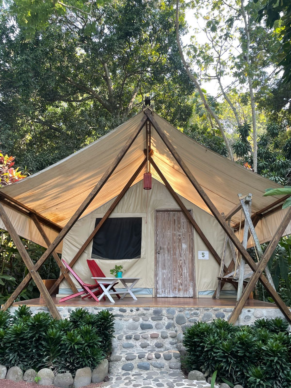Una carpa con una escalera de piedra que lleva a una puerta, rodeada de vegetación.