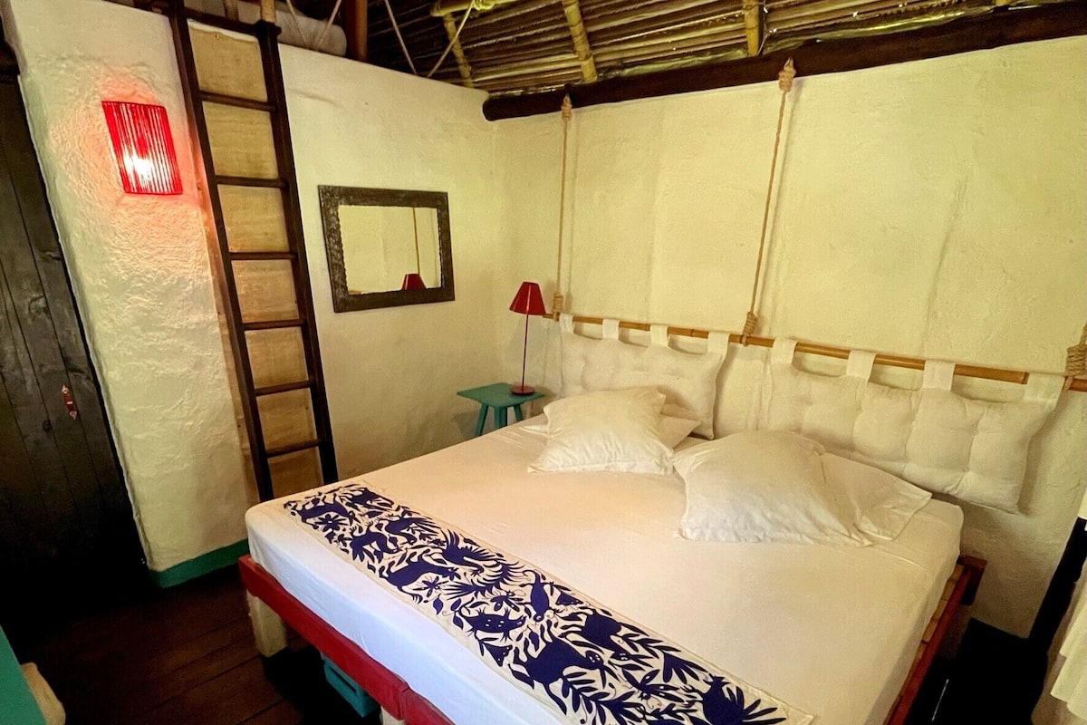 A single-bed room with a wooden headboard, a small bedside table with a lamp, and a mirror on the wall.
