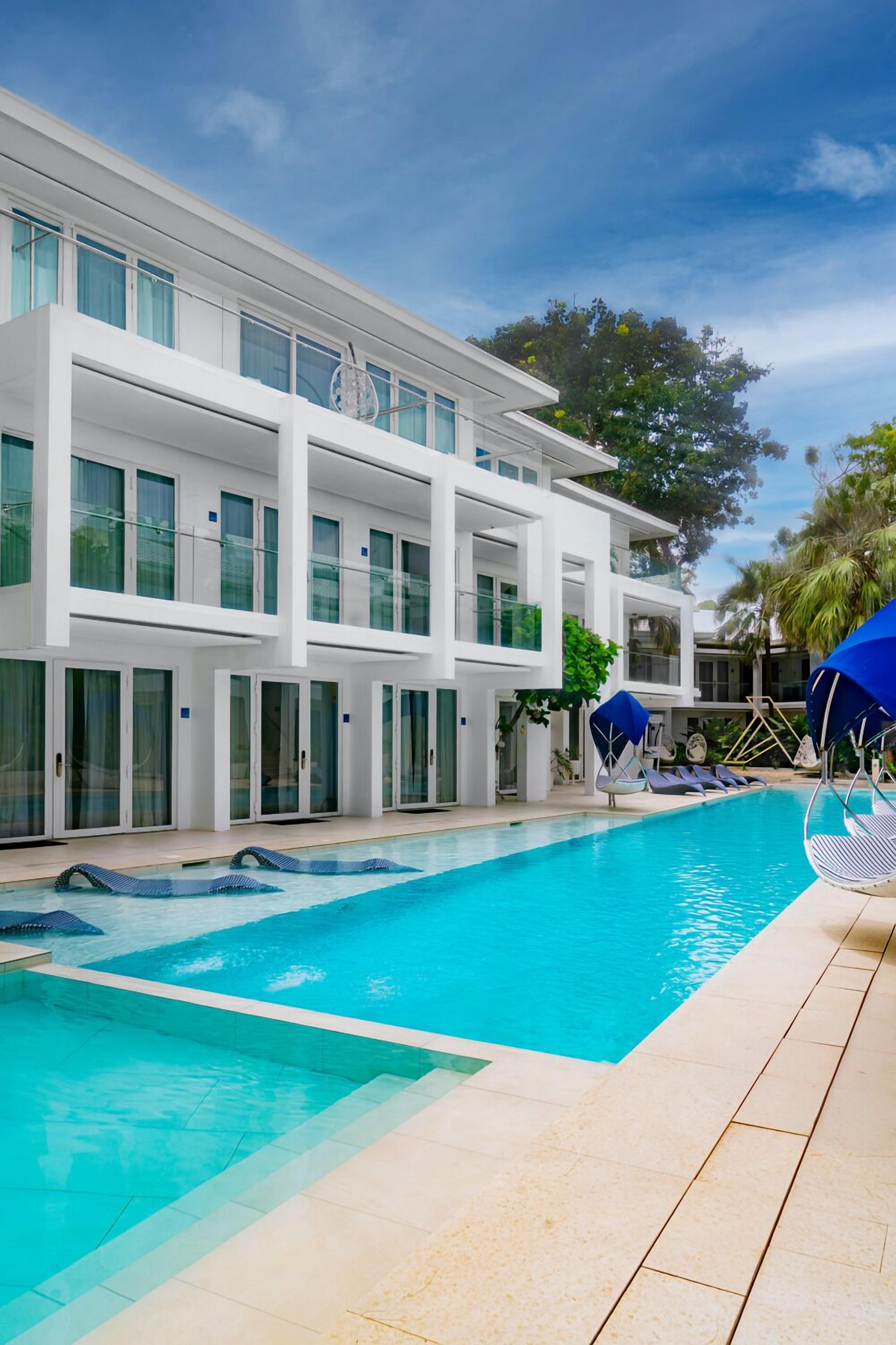 Una piscina al aire libre, sombrillas, sillones reclinables de piscina