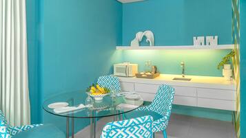 Una cocina moderna con una mesa de comedor de cristal, sillas azules con estampado y una encimera blanca con microondas y tostadora.