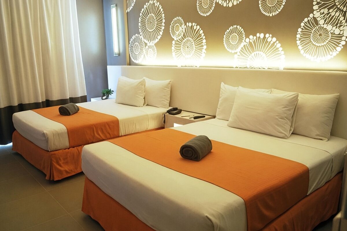 Quarto de hotel com duas camas, cada uma com colcha laranja e almofadas brancas.