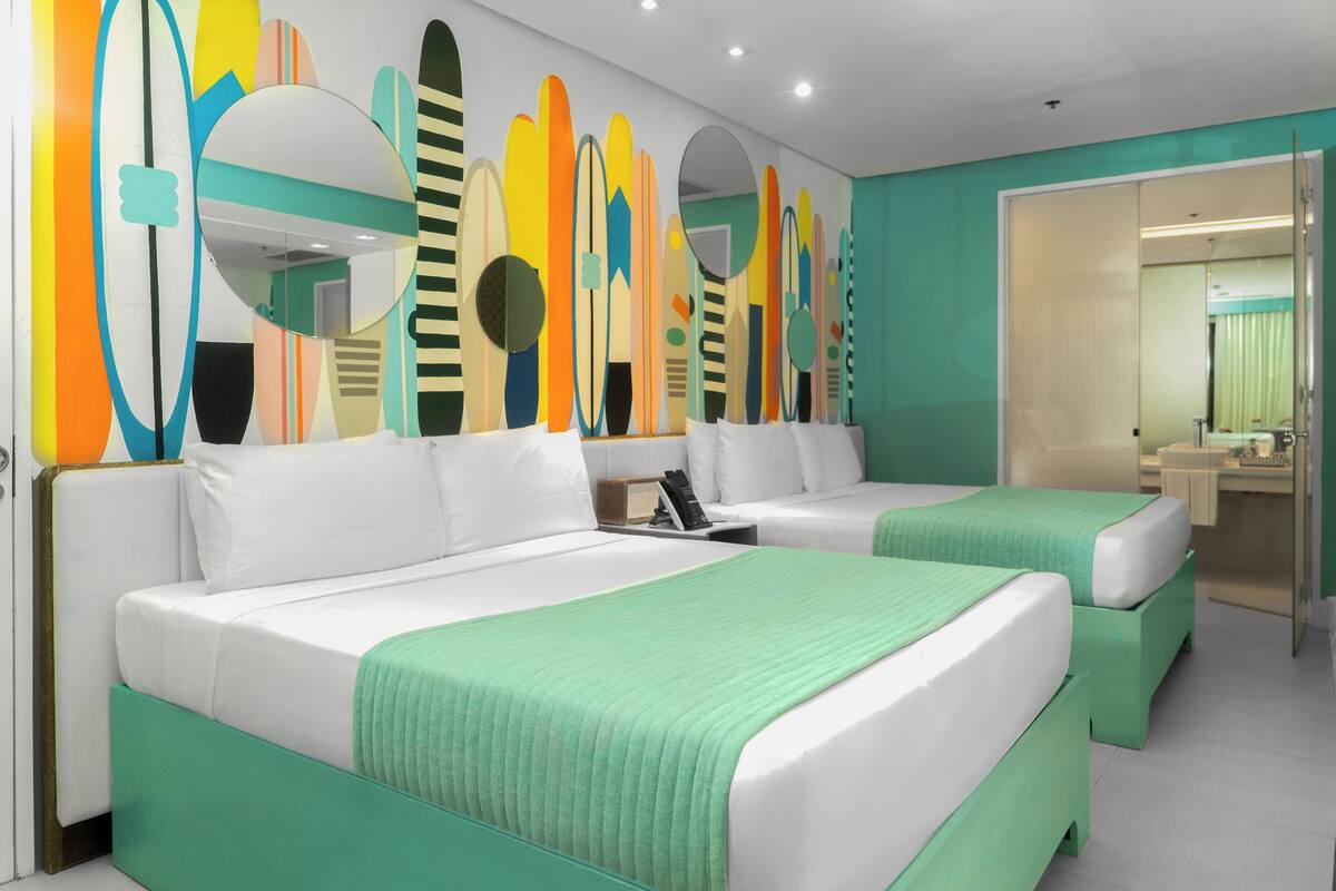 Ein Hotelzimmer mit zwei Betten, einem Badezimmer und einer Wand mit Surfboard-Motiven.