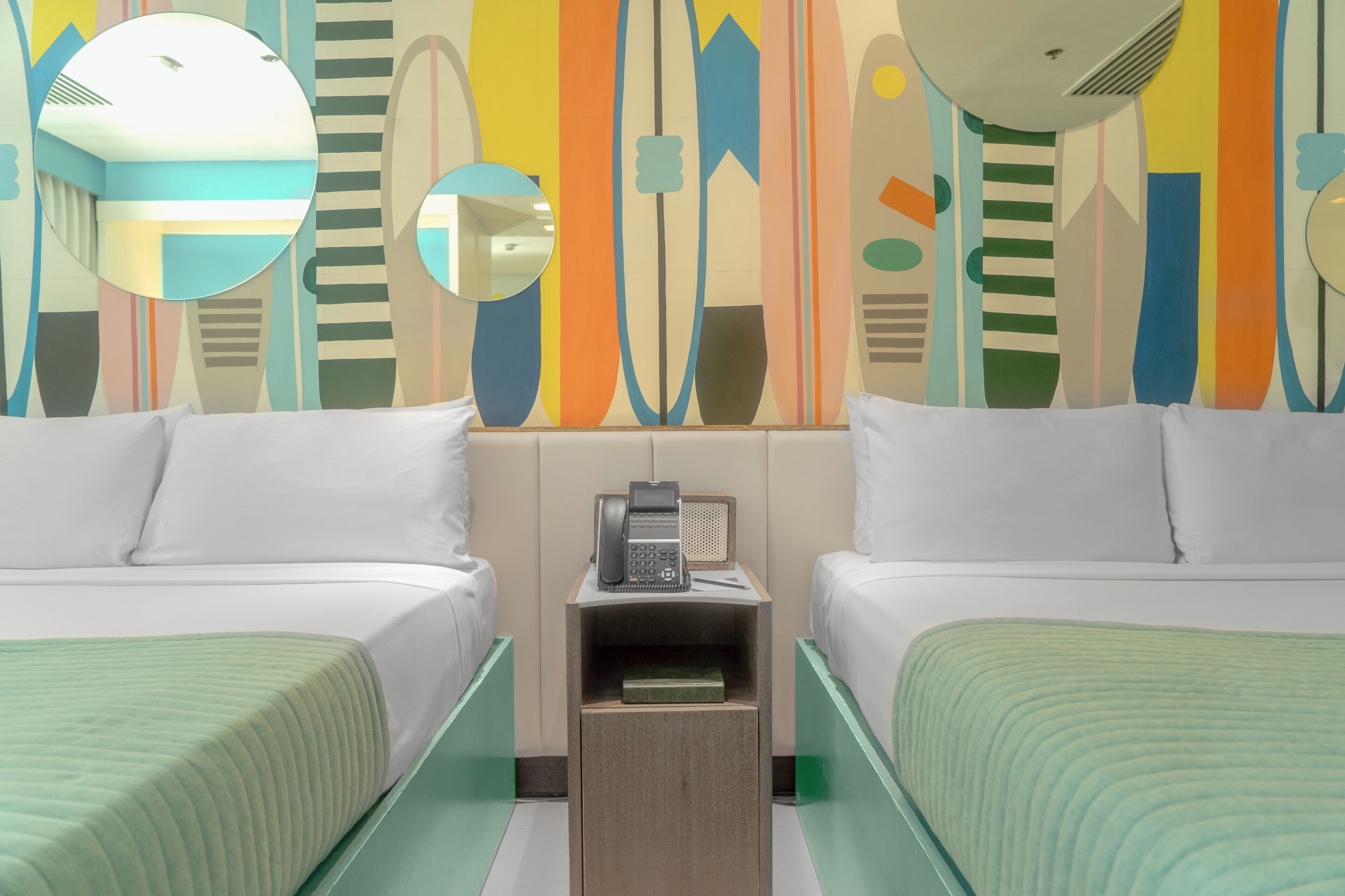 A hotel room with two beds, a small table with a telephone, and a wall with abstract art.