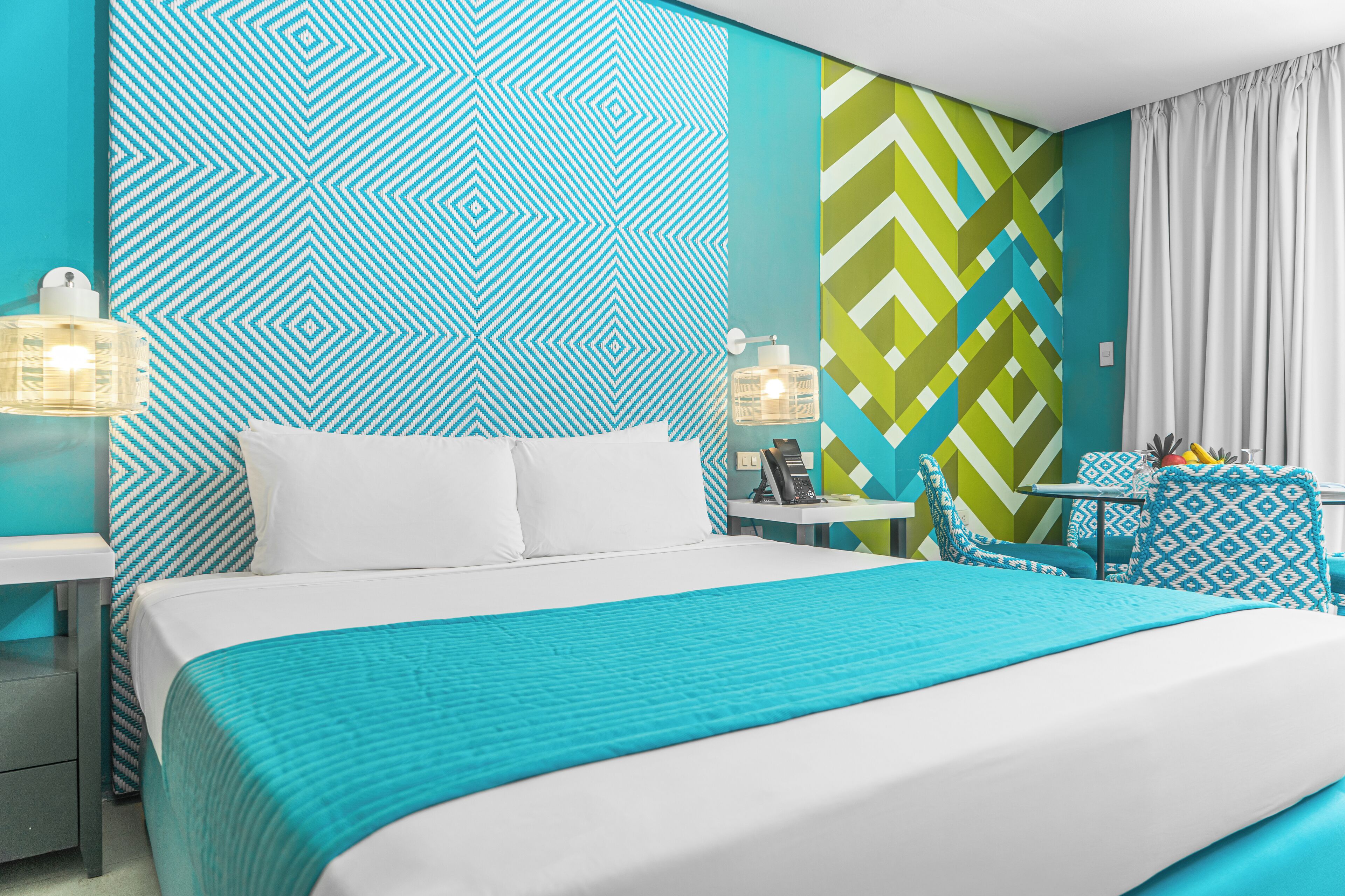 A hotel room with a large bed, a nightstand, a table with chairs, and a patterned wall.