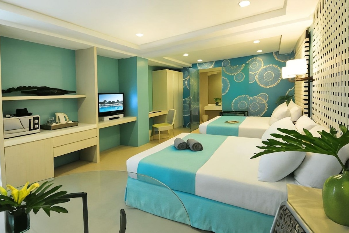 Quarto de hotel moderno com duas camas, uma escrivaninha, televisão e banheiro.
