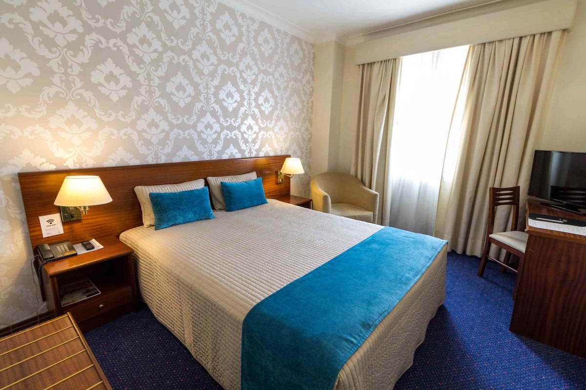 A hotel room with a large bed, two bedside lamps, a desk with a TV, and a chair.