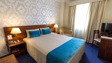 Een hotelkamer met een groot bed, twee bedlampen, een bureau met een televisie en een stoel.