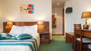 Een hotelkamer met een bed, twee bedlampen, een bureau met stoel en een tapijt met een groen patroon.