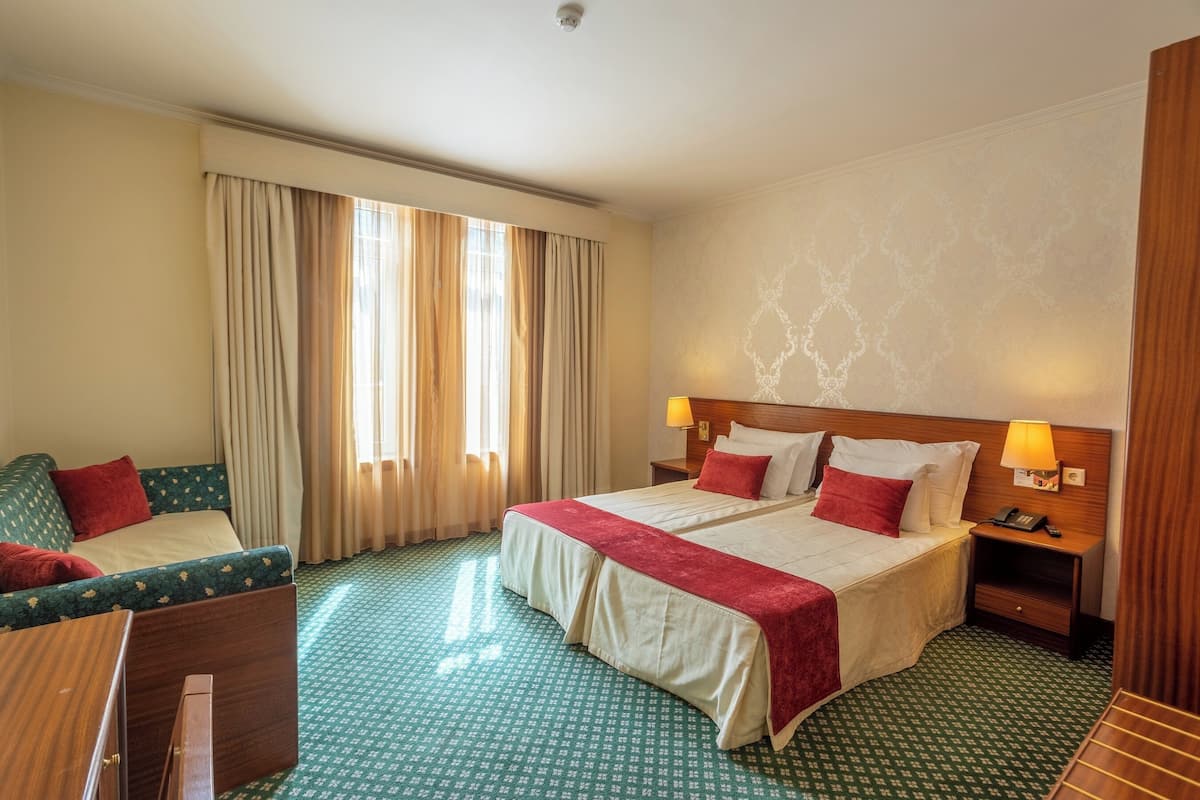 A hotel room with two beds, a desk, a chair, and a window with curtains.