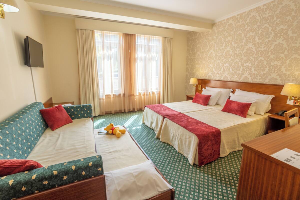 A hotel room with two beds, a sofa, a desk, and a television.