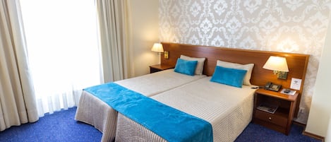 Habitación de hotel con una cama grande, dos mesitas de noche con lámparas, un aparador y una ventana con cortinas.