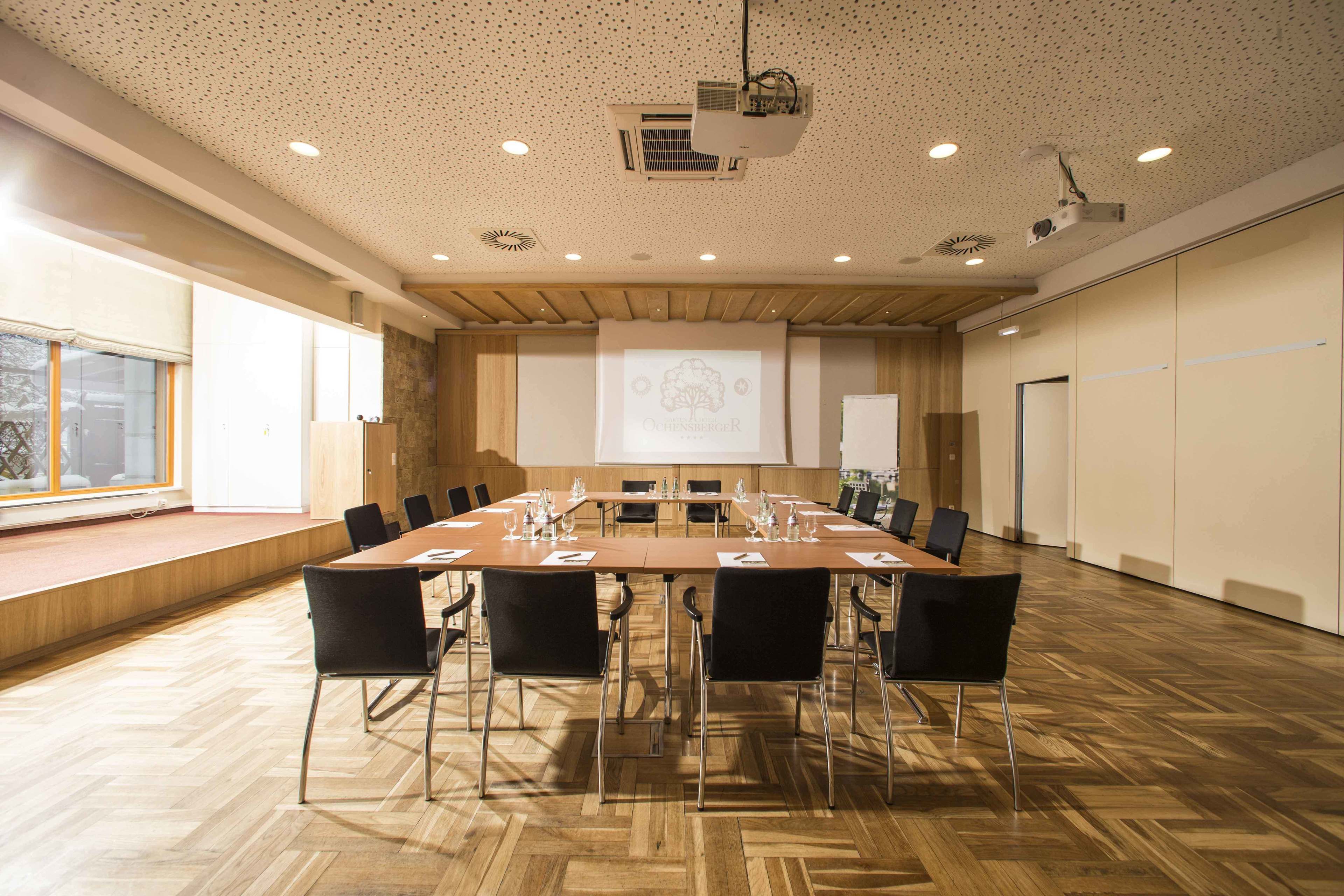 A conference room with a large table, chairs, a projector screen, and a presentation on the wall.