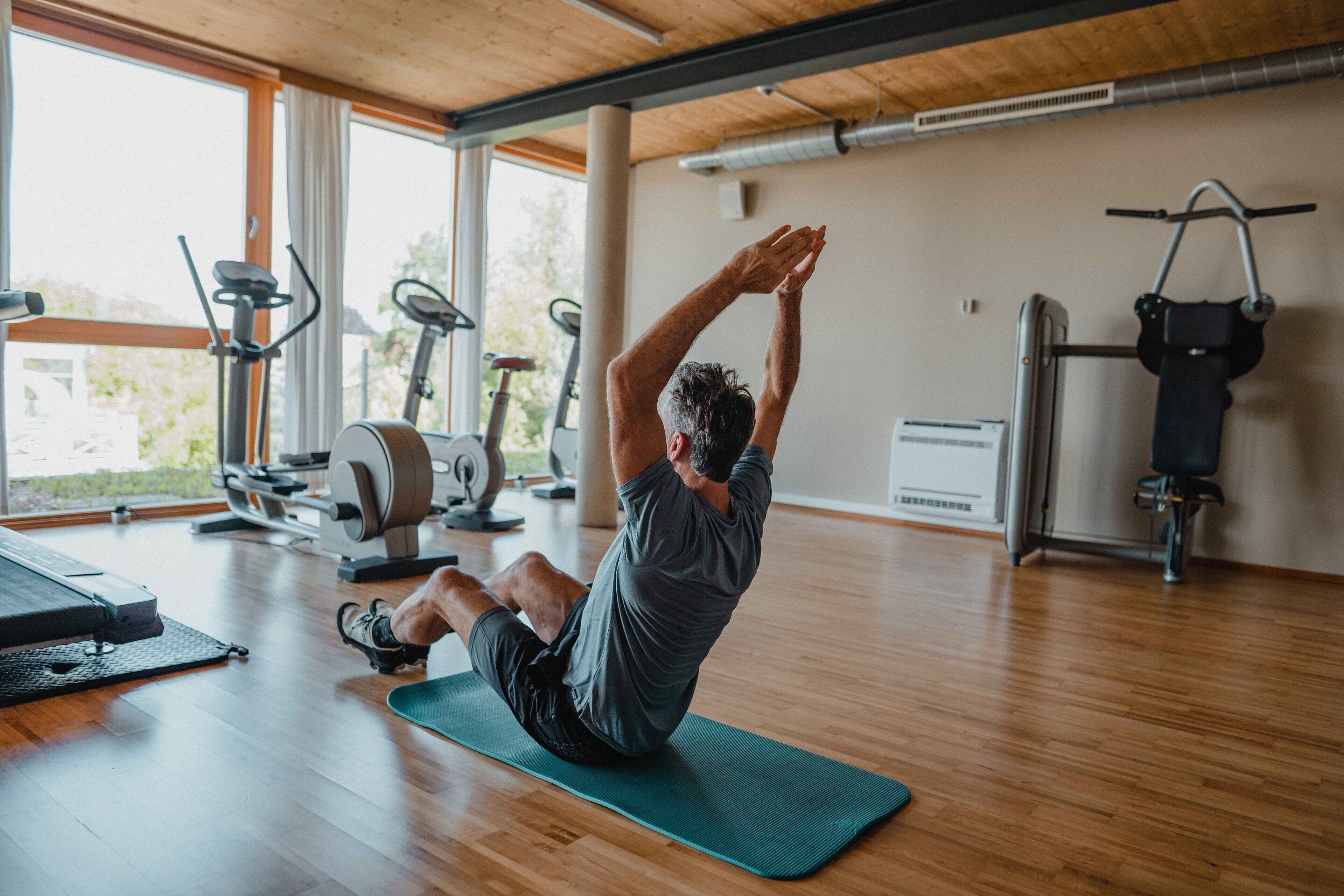 Un gimnasio con equipo de ejercicio, piso de madera y ventanas amplias.