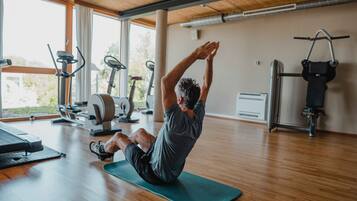 Un gimnasio con equipo de ejercicio, piso de madera y ventanas amplias.