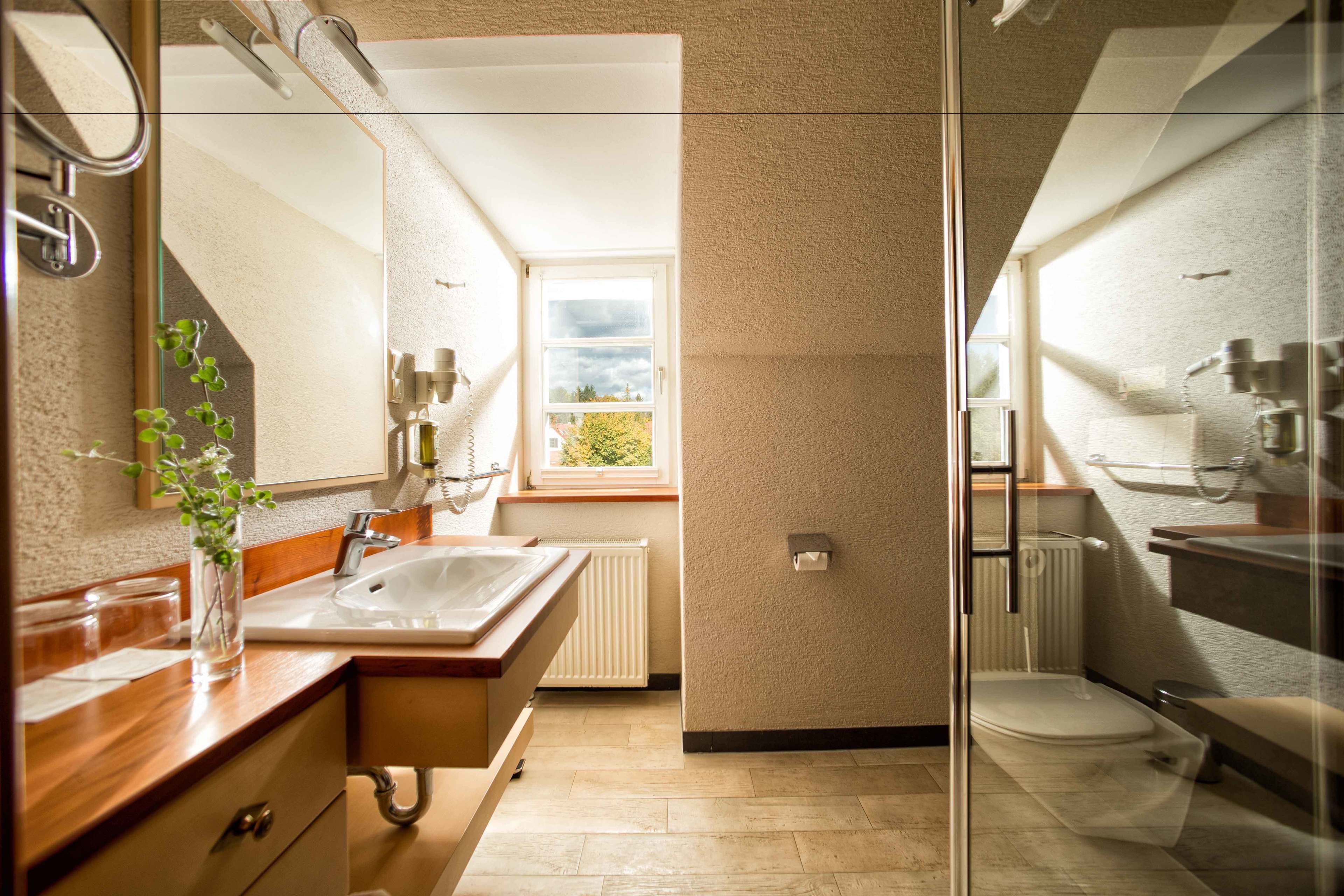 A modern bathroom with a wooden vanity, a large mirror, a window, and a glass shower enclosure.