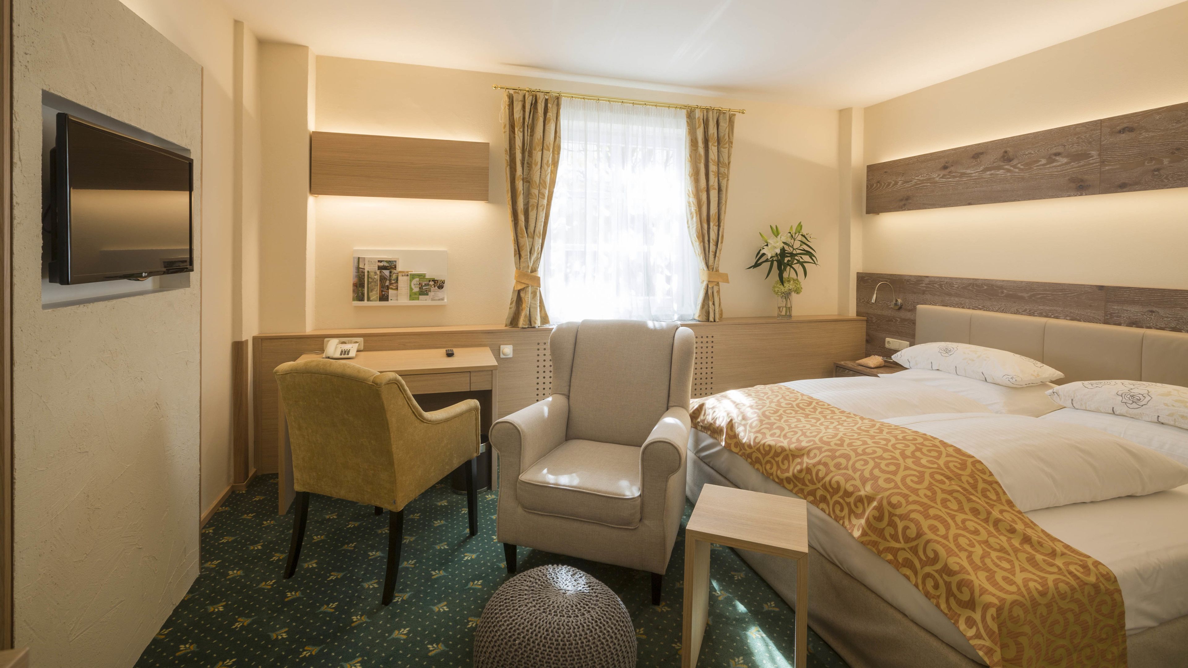 Habitación de hotel con cama, escritorio, silla, televisión y una planta.