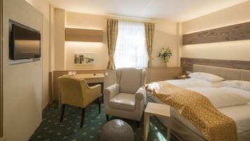 Habitación de hotel con cama, escritorio, silla, televisión y una planta.