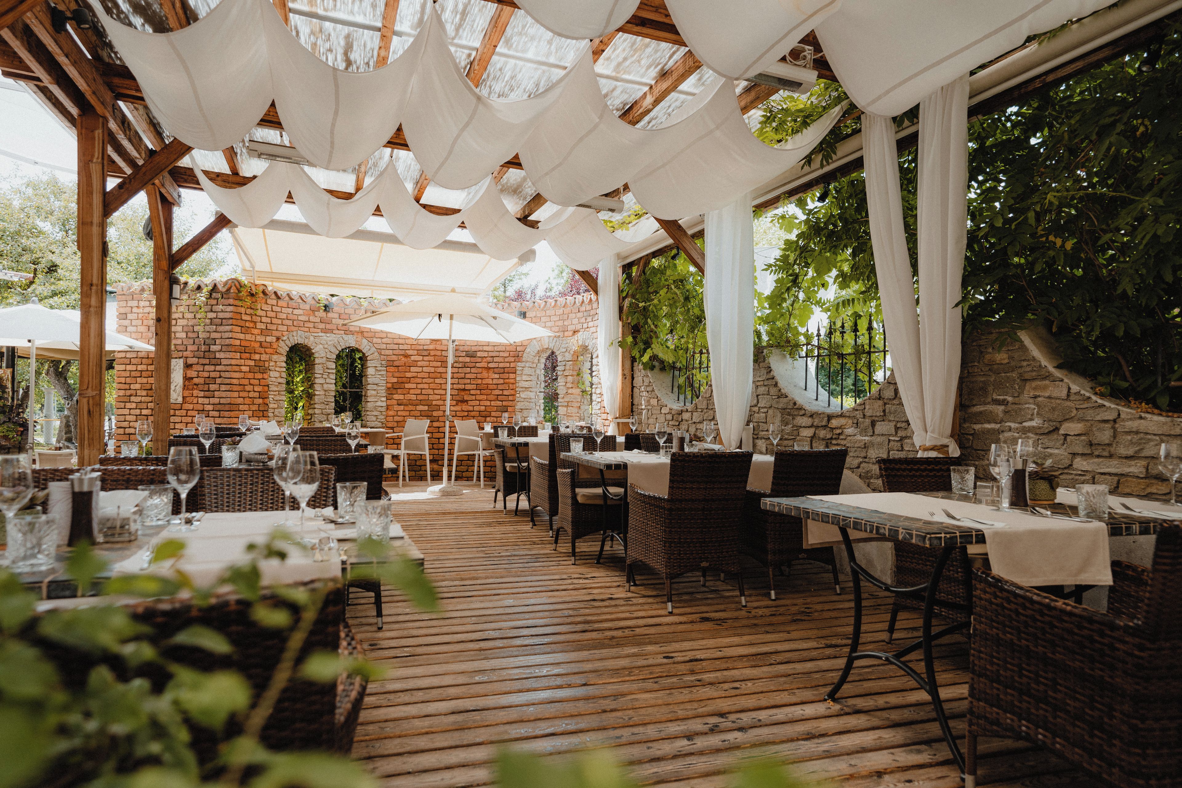 Un espace extérieur aménagé pour les repas, avec des murs en briques, un plancher en bois et des tables dressées.