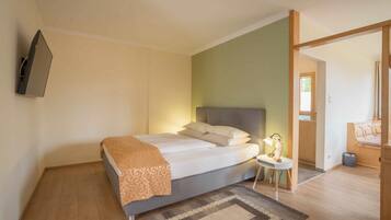 A bedroom with a bed, bedside table, lamp, and a TV mounted on the wall.